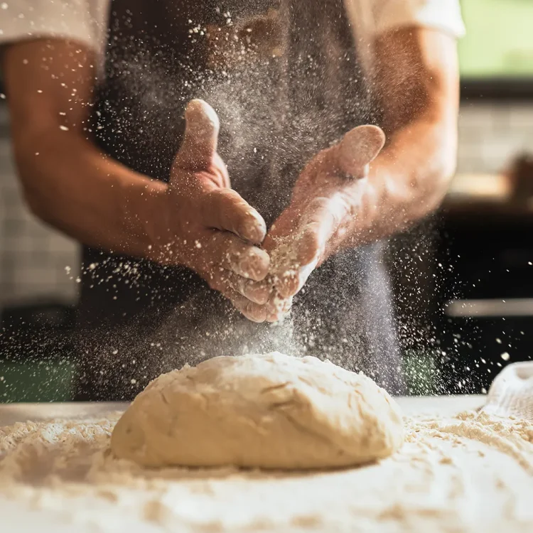 Männerhände mit Mehlstaub über einem Teig-klumpen auf einer Arbeitsplatte - Privatköch:in