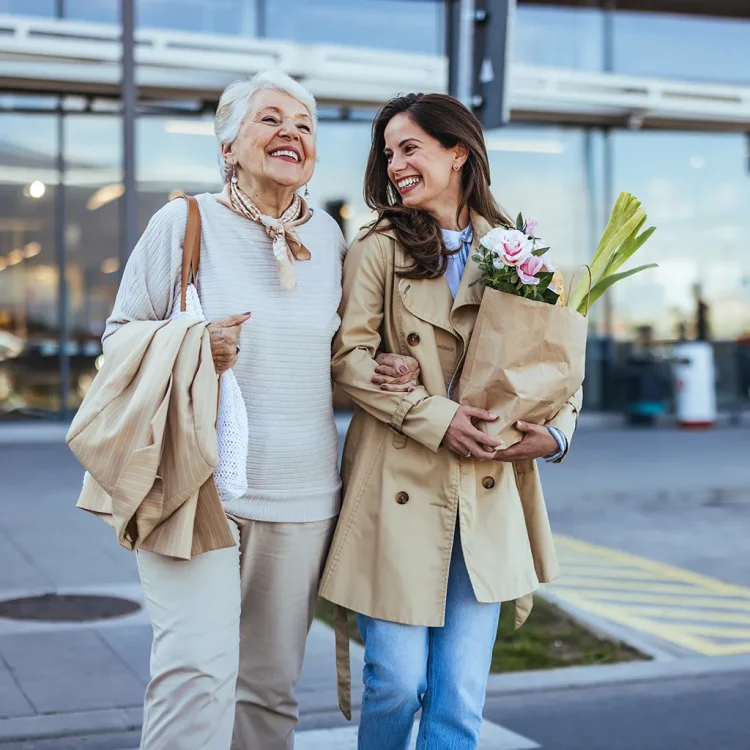 Ältere Frau und Junge Frau lachen zusammen, Junge Frau trägt Tüte mit Lebensmitteln